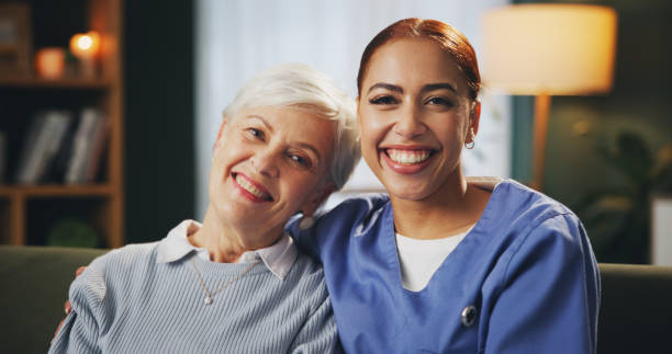 Home, senior woman and nurse in portrait for hug, caring and support in retirement with happiness. Lounge, elderly patient and female caregiver with embrace on sofa, assistance and medical volunteer